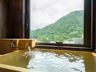 【天然温泉客室ヒバ風呂(渓谷側)】窓から移ろう景色を眺めながら、気の向くままに何度でも湯浴みをお愉しみいただけます。