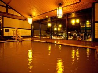 【大浴場/内湯】灯りに合う茶褐色の湯は美肌効果も。窓から見える夜景に心も癒されながら…